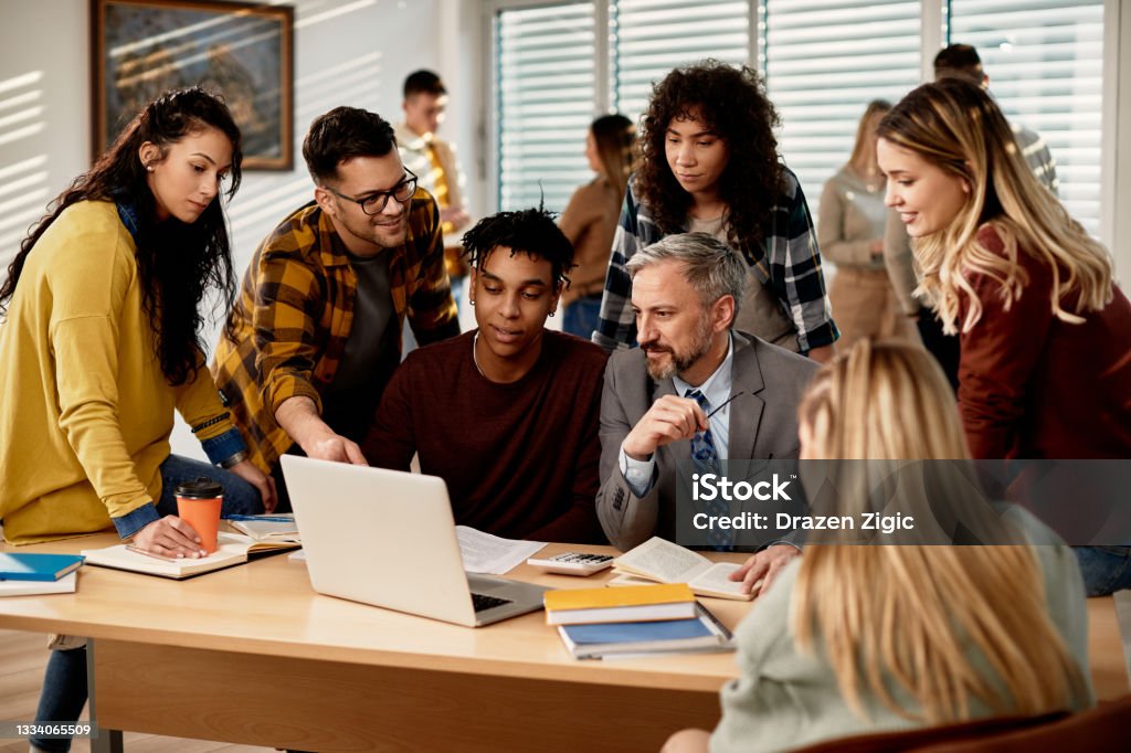Mature teacher and group of his students using laptop at the university,