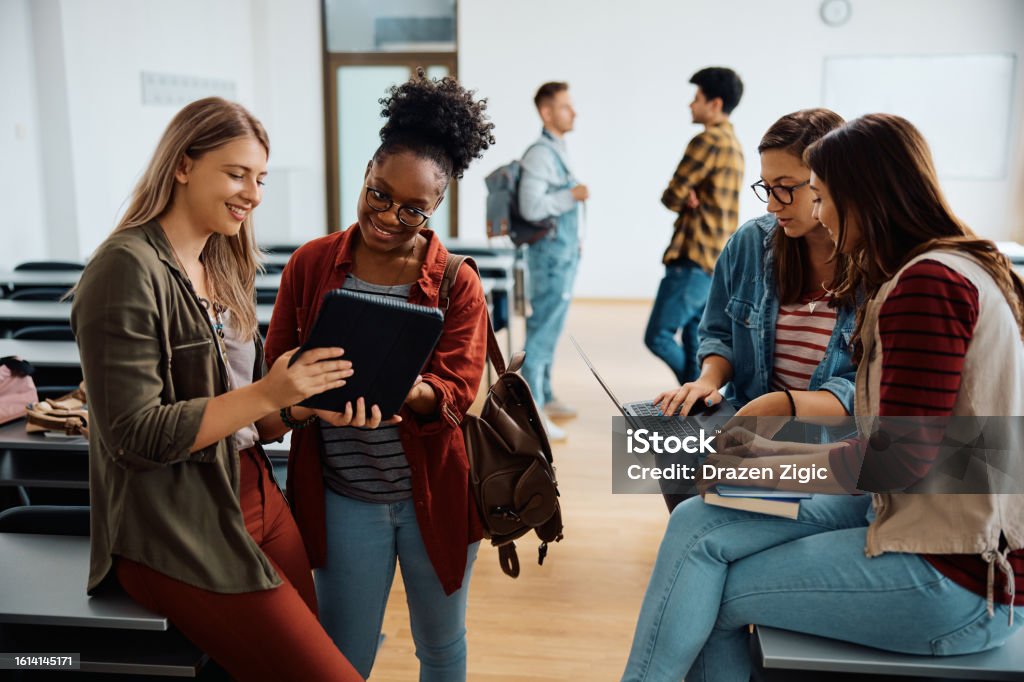 Happy female friends e-learning while using wireless technology at university classroom.